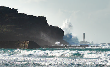 Longships cliffs waves This landscape photograph captures dramatic waves crashing against the Longships cliffs on the coast of Cornwall, United Kingdom, during the early afternoon in winter. The rugged cliffs of Sennen Cove rise prominently on the left of the image, while the powerful sea surges ashore, sending plumes of spray into the air. In the distance, the Longships Lighthouse stands as a landmark, watching over the tumultuous waters of this section of the Cornish coast. The winter light highlights the natural features of the cliffs, the dynamic motion of the sea, and the enduring presence of the lighthouse, all characteristic of this wild part of nature in the United Kingdom.